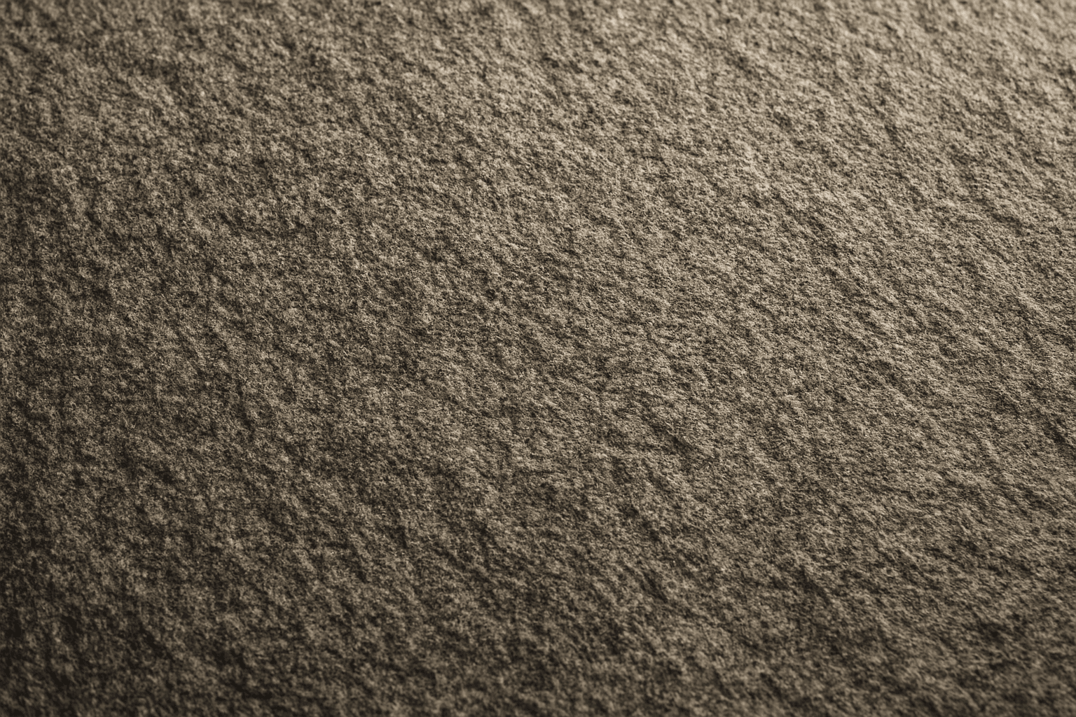 Close-up of a natural stone surface showing fine granular texture with subtle light and shadow
